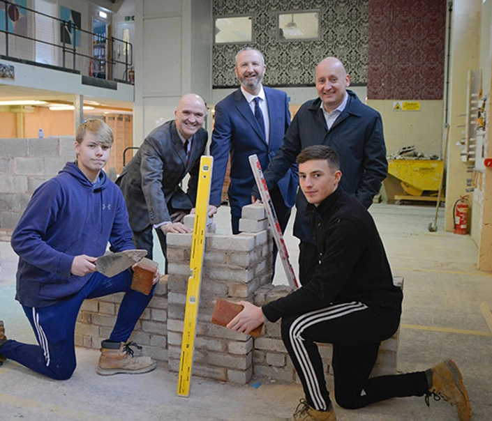 students and staff around partially built wall