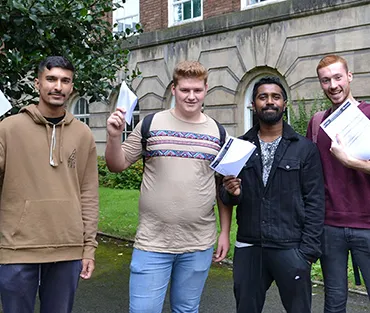 Four students standing in front of college with certificates