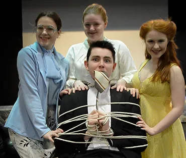 Three students surround seated student tied up in chair 