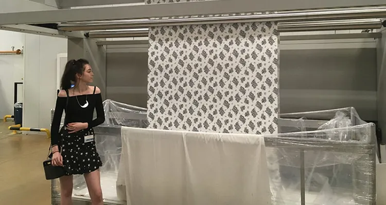 Art and design student standing in front of fabric printing press with her design being printed