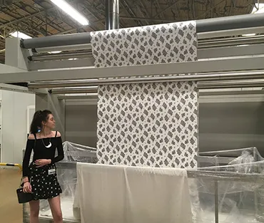 Art and design student standing in front of fabric printing press with her design being printed