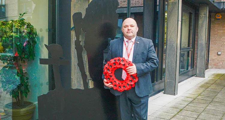 College Commercial Manager holding a poppy wreath and standing next to wooden silhouette of a soldier