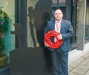 College Commercial Manager holding a poppy wreath and standing next to wooden silhouette of a soldier