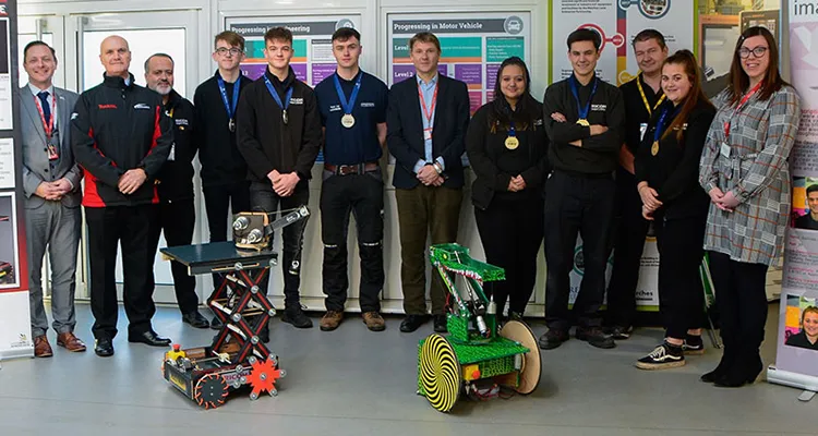 A group of apprentices, College staff, including the Principal and employers standing behind two robots